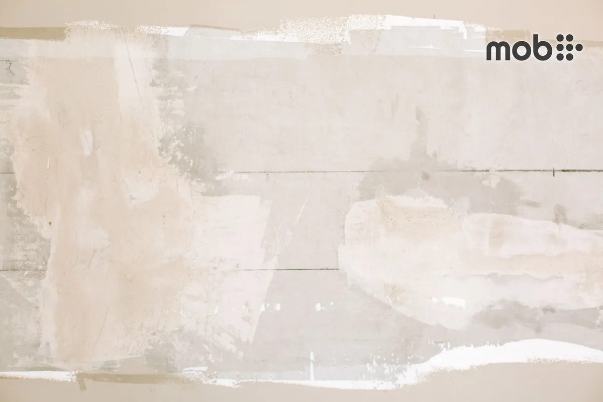 Painter applying white cement wall putty evenly on an interior wall with a putty blade
